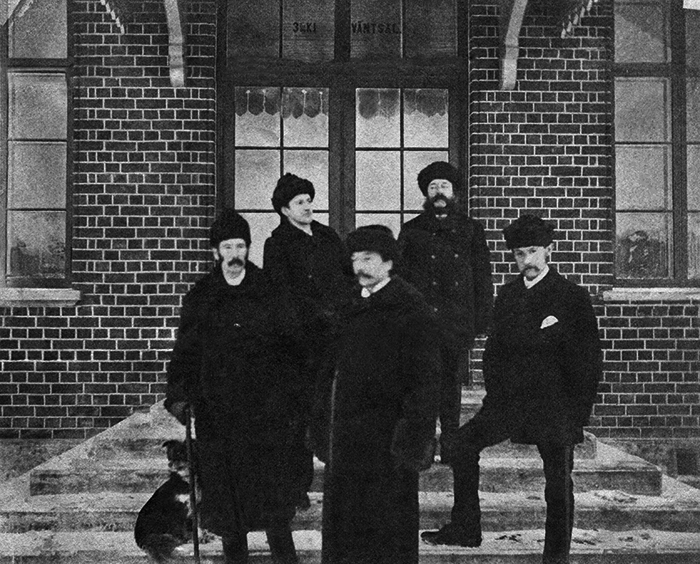 Fem vinterklädda herrar vid stationshustrappa.